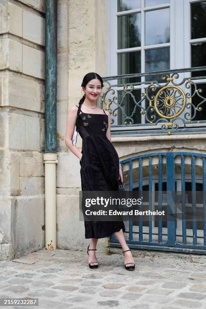 Ora Yang wears silver hoop earrings, silver necklace, black midi dress with silver butterflies embroidered, gold bracelet, silver ring, black and...
