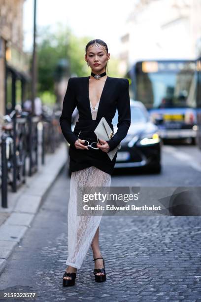 Lucy Qiu wears silver earrings, black choker with silver pendant, white deep v-neck sheer mesh lace pattern maxi dress, black blazer jacket mini...