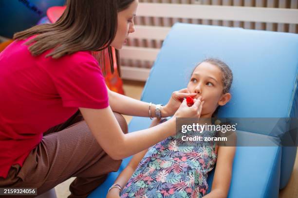girl patient doing breathing exercise with party horn assisted by female specialist - atrophy stock pictures, royalty-free photos & images
