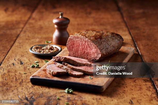 succulent medium rare beef roast on a rustic wooden board with seasoning - foodstyling stockfoto's en -beelden