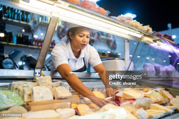 woman arranging the cheese refrigerator display at a delicatessen - grocer stock pictures, royalty-free photos & images