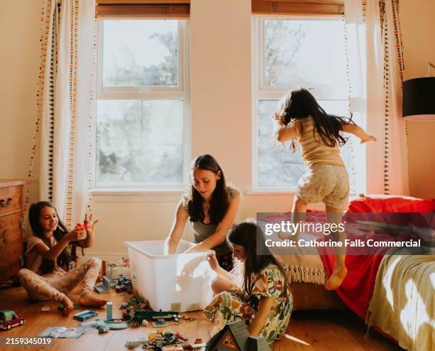 a loving mother plays with a box of toys with her three young daughters - amontoar imagens e fotografias de stock