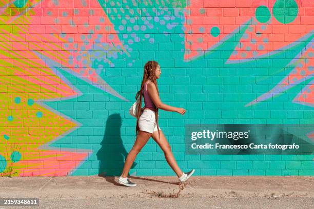 woman with braided hair walking by multicolored design wall - confident woman walking side view stock pictures, royalty-free photos & images