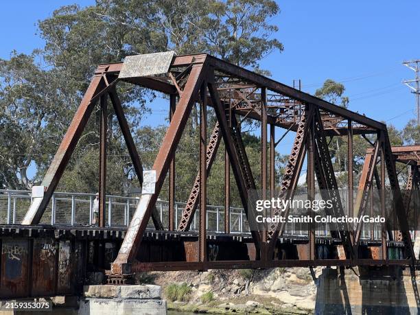 Rustic iron San Lorenzo River Railroad Bridge with graffiti and pedestrian walkway on a sunny day, Santa Cruz, California, June 22, 2024.