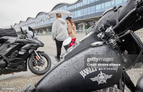 June 2024, Hamburg: Visitors walk past motorcycles with umbrellas during the Hamburg Harley Days at the wholesale market. Photo: Georg Wendt/dpa