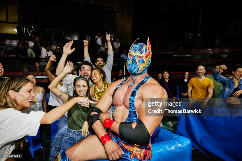 Medium wide shot luchador posing with cheering fans in stadium