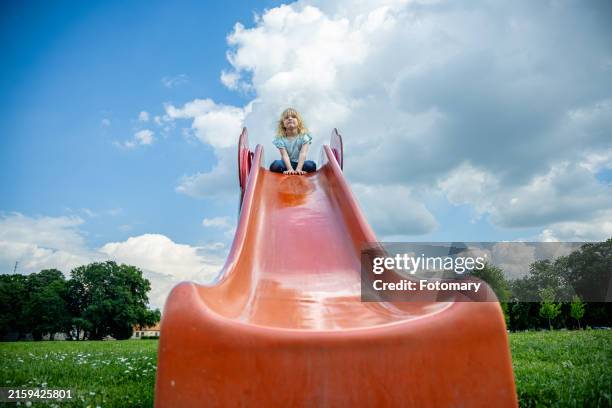 joyful girl slides down a bright orange slide in a playground. - rutsche stock-fotos und bilder