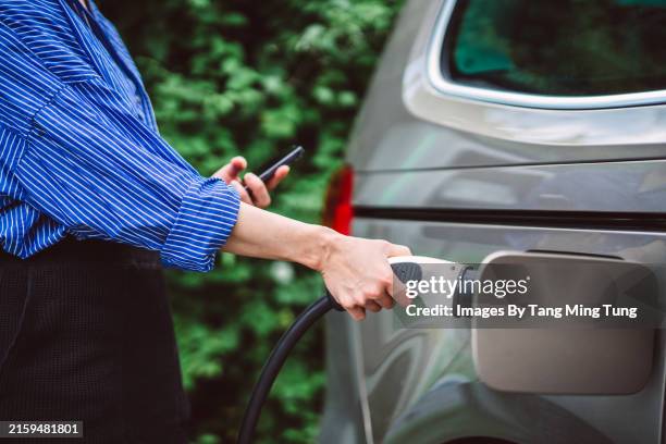 young businesswoman charging her electric car at ev charging station - electric car stock pictures, royalty-free photos & images