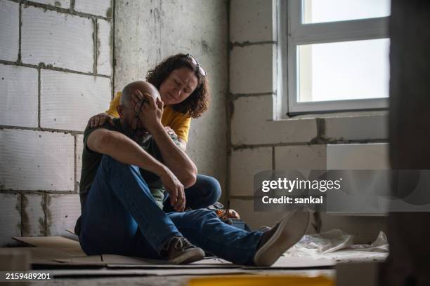 a woman consoling husband sitting on floor in the house under construction - construction mistake stock pictures, royalty-free photos & images