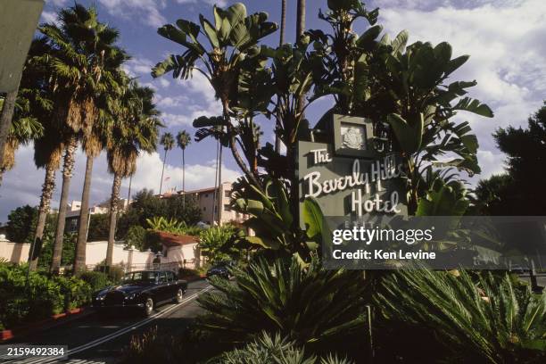 An exterior view of palm trees surrounding the hotel sign and driveway with a Rolls Royce on the exit ramp of the Beverly Hills Hotel circa October...