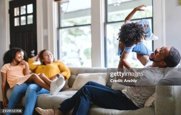 joyful parents sitting on the sofa with their cute kids - comfortabel stockfoto's en -beelden
