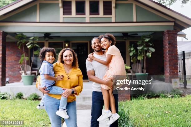 portrait of parents holding their two kids in front of the house - proprietario di casa foto e immagini stock