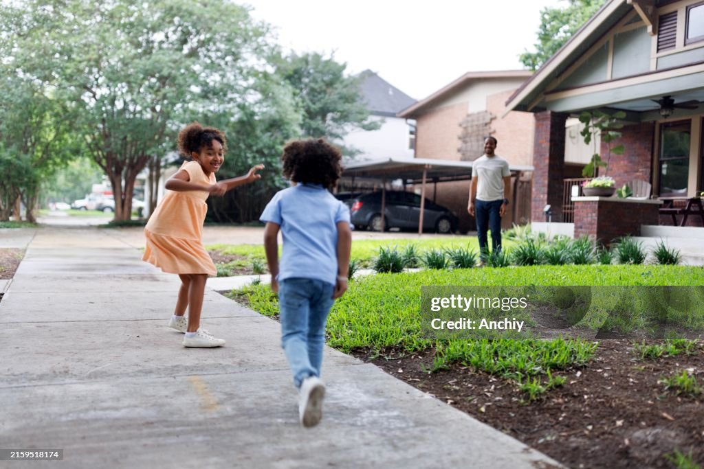 Siblings playing tag game in front of their house