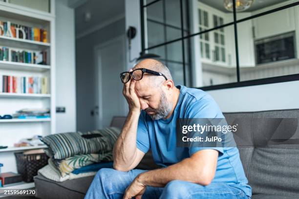 mature adult man with depression sitting on sofa at home - moe stockfoto's en -beelden