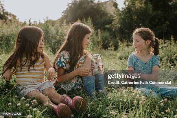 three little girls sit outside on the grass on a sunny evening - endast flickor bildbanksfoton och bilder