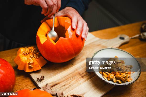 man hands taking out seeds from pumpkin while carving jack o lantern for halloween - pumpkin seed stock pictures, royalty-free photos & images