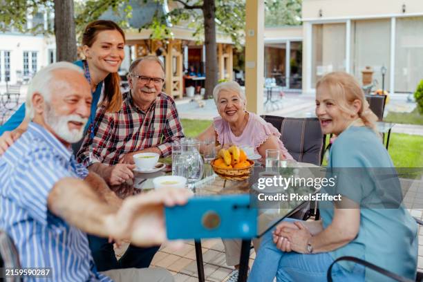 personas mayores con enfermera tomando selfie mientras disfrutan juntos en un hogar de ancianos - joven de espíritu fotografías e imágenes de stock