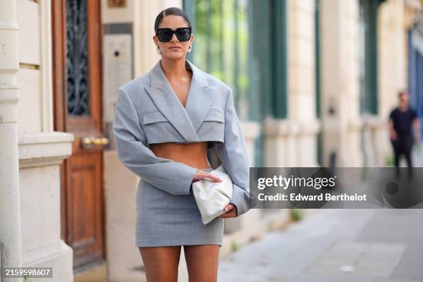 Gili Biegun wears black sunglasses, silver earrings, light gray cropped blazer jacket, light gray mini skirt, white leather handbag, outside...
