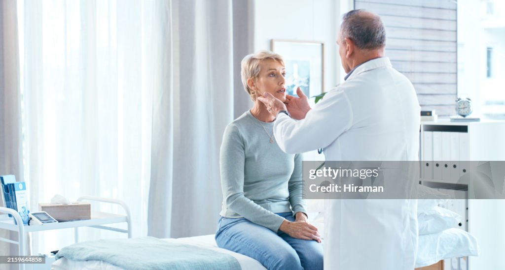 Ein leitender Arzt untersucht eine ältere Patientin in einer gut beleuchteten Arztpraxis. Der Arzt scheint den Hals der Patientin zu untersuchen, während sie auf dem Untersuchungstisch sitzt.