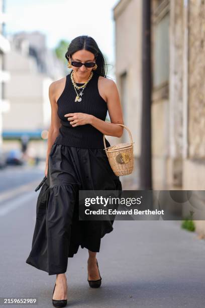 Guest wears black sunglasses, gold earrings, gold necklace, silver layered necklaces, a gold ring, black pattern tank top, black button up flowy midi...