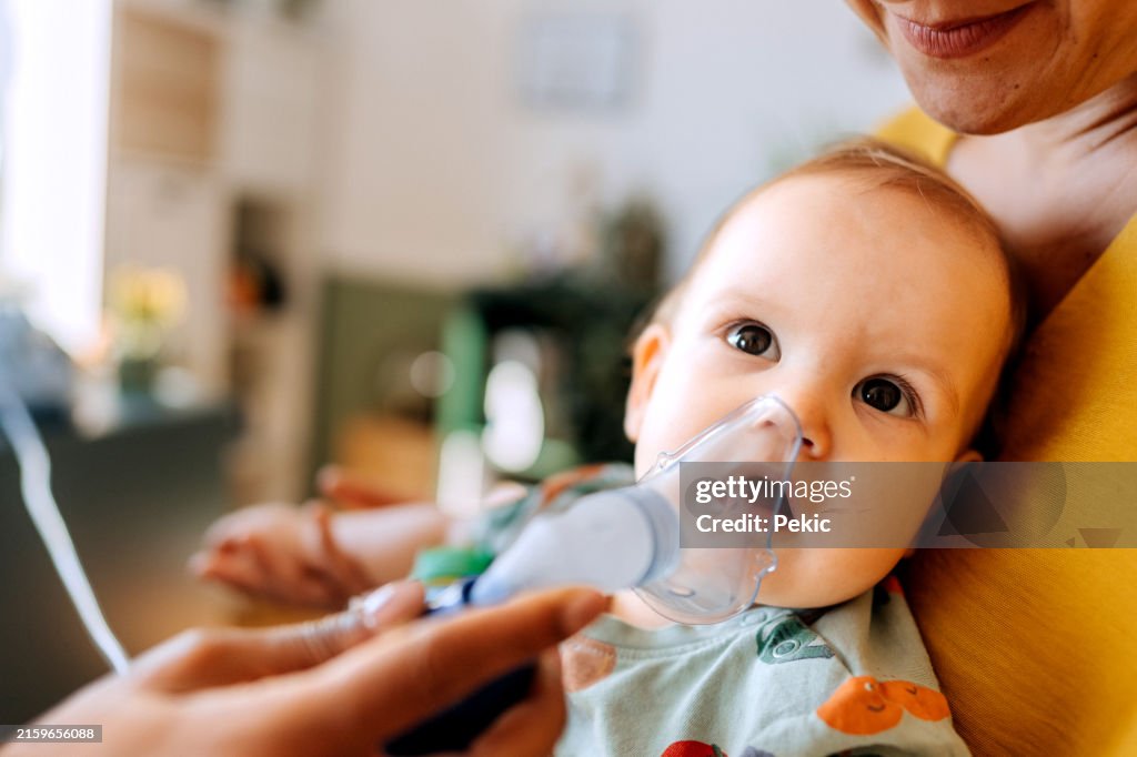 Kinderärztin inhaliert kleinen Jungen mit Vernebler-Inhalator-Gesichtsmaske, während seine Mutter ihn auf dem Schoß hält
