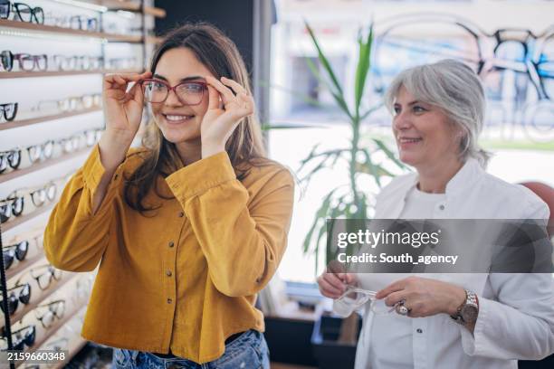 junge frau im gelben hemd probiert roten brillenrahmen aus - augenuntersuchung stock-fotos und bilder