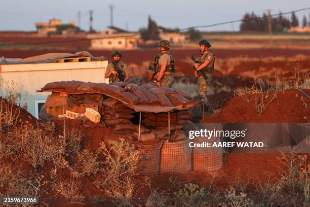 Turkish army soldiers stand guard at an observation point as Syrian demonstrators gather nearby in Ibbin Samaan in the western part of Syria's...