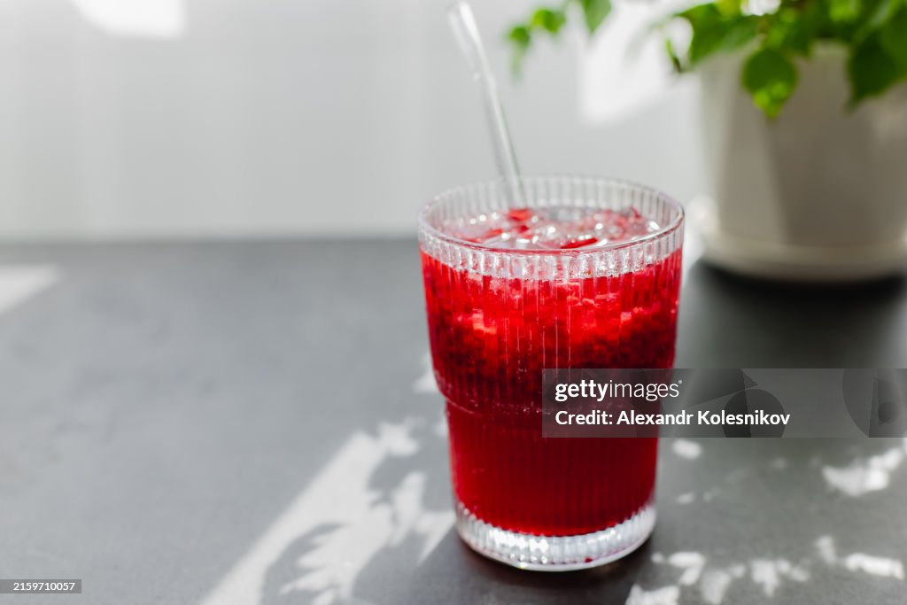 Summer drink. Glass with raspberry lemonade with glass straw on dark table with sunlight. Copy space