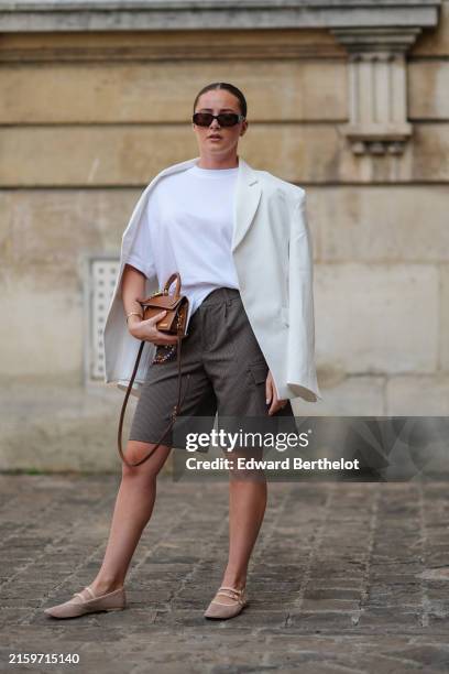 Guest wears black sunglasses, white oversized cotton t-shirt, white linen oversized blazer jacket, dark gray pattern high waisted shorts, dark brown...