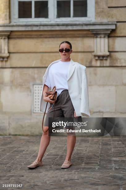 Guest wears black sunglasses, white oversized cotton t-shirt, white linen oversized blazer jacket, dark gray pattern high waisted shorts, dark brown...