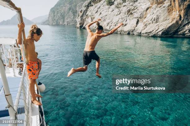 happy boys jumping from boat at sea against sky. children jumping in the water from boat. - greece stock pictures, royalty-free photos & images