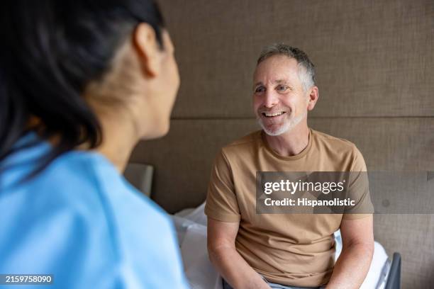 mature man talking to a nurse in assisted living facility - medical clinic stock pictures, royalty-free photos & images