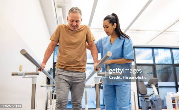 man in physical therapy walking on the bars with assistance of his therapist - fysiotherapie stockfoto's en -beelden