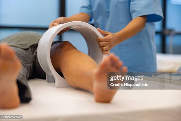 physical therapist applying magnetic field therapy on the knee of a patient - magnetisch veld stockfoto's en -beelden