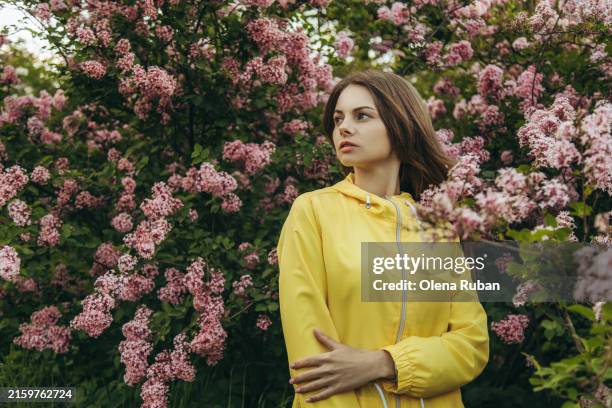 beautiful woman in a raincoat standing among lilac flowers in a garden. - purple lilac stock pictures, royalty-free photos & images