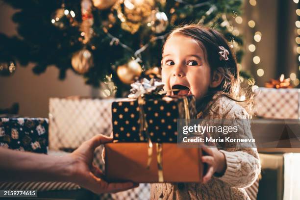 lovely little girl receiving a christmas gift. - regalo di natale foto e immagini stock
