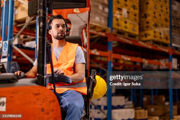trabajador masculino feliz conduciendo carretilla elevadora en almacén de distribución - carretilla elevadora fotografías e imágenes de stock