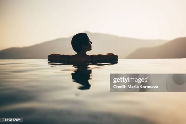 young woman enjoying the magical view in the infinity pool at sunset. - poolside stock pictures, royalty-free photos & images