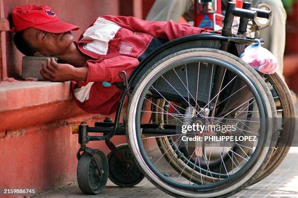 Handicapped Cambodian man sleeps 16 March 2000 in his wheelchair in the shade of the Phnom Penh's National Museum, where he came to beg money like...