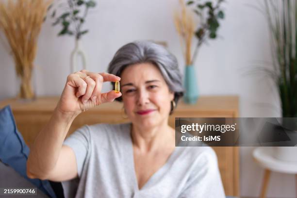 senior woman holding a pill of omega 3 fatty acids - omega 3 stock pictures, royalty-free photos & images