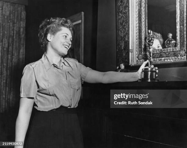 American actress, singer and comedian Judy Holliday admires her 'Best Actress' Oscar on the mantelpiece in her Greenwich Village apartment, in Lower...