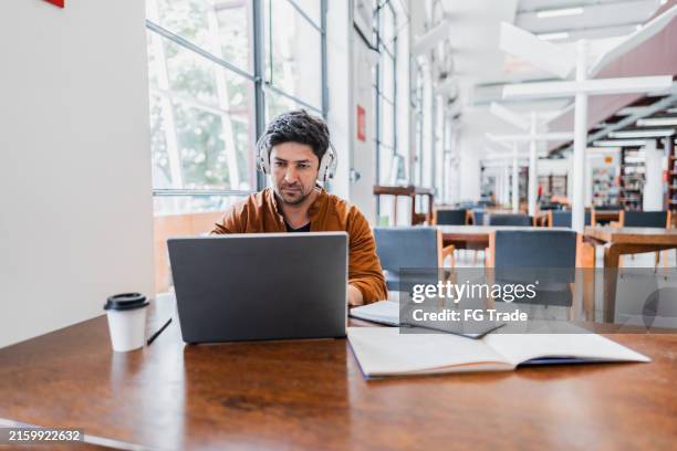 mid adult man working using laptop at library - master of business administration stockfoto's en -beelden