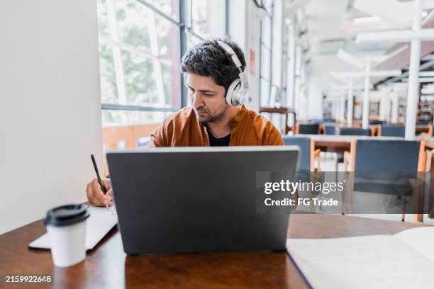 mann im mittleren erwachsenenalter, der mit laptop in der bibliothek arbeitet - online lernen stock-fotos und bilder