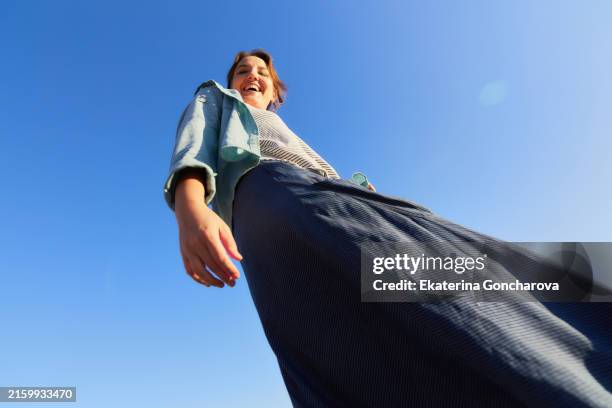low-angle shot of a woman smiling and looking down against a clear blue sky. - gran angular fotografías e imágenes de stock