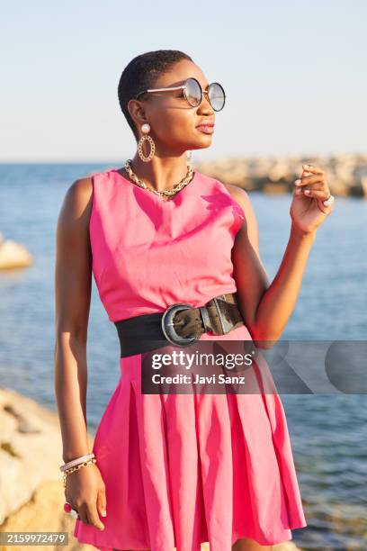 modelo femenina negra con el pelo corto posando con un vestido rosa y gafas de sol - vestido rosa fotografías e imágenes de stock