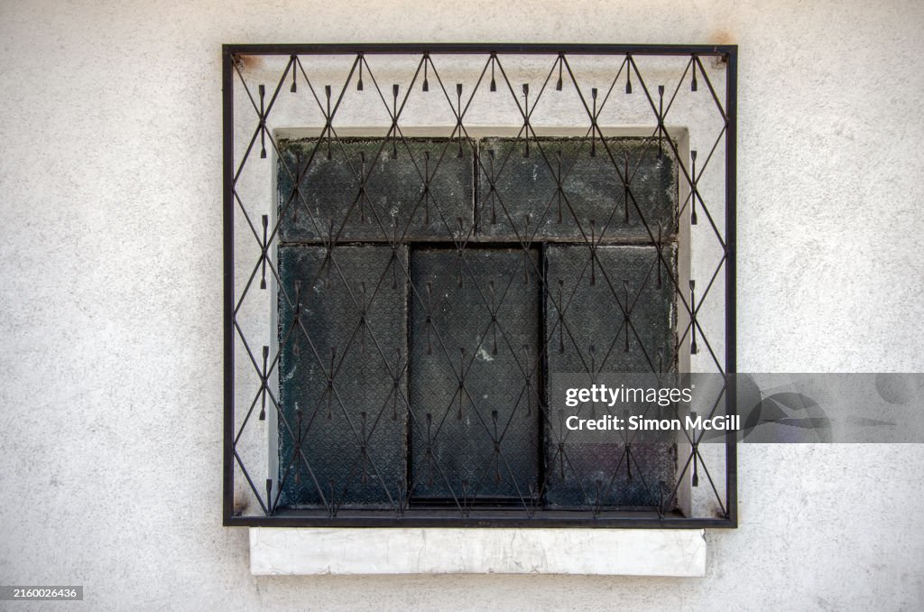 Diamond-shaped wrought iron patterned security grill over a window on a colonial-style house