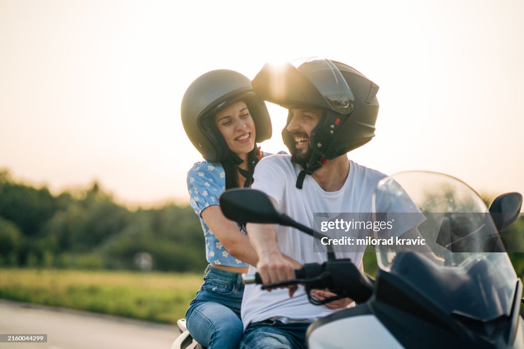 Happy young couple riding on a motorcycle on the road in nature