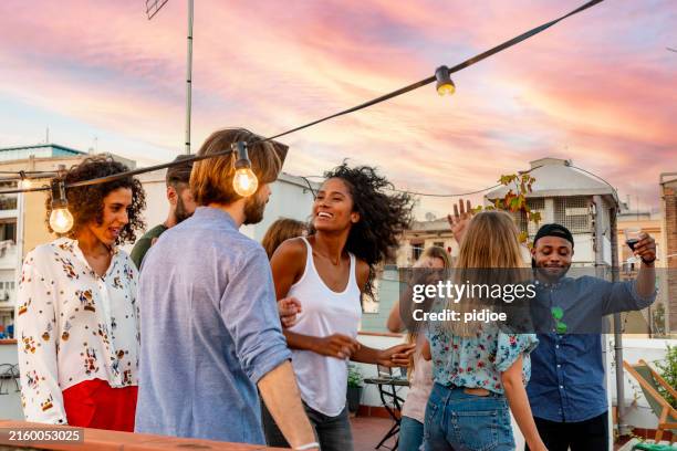 young adults celebrating life and friendship on a rooftop in barcelona, spain. candid shot of eight young friends having fun on a rooftop party - hipster stock pictures, royalty-free photos & images