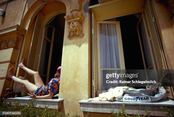Christina de Caraman-Chimay relaxes in the sun while her boyfriend, Francois Cevert, takes a shower after a practice session leaving his overalls to...