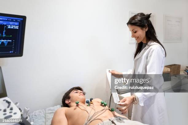 kardiologe, der ein elektrokardiogramm an einem jugendlichen patienten durchführt - echokardiogramm stock-fotos und bilder